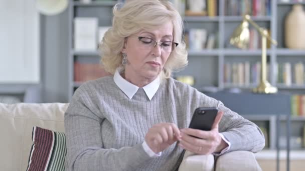 Alte Frau benutzt Smartphone auf dem Sofa — Stockvideo