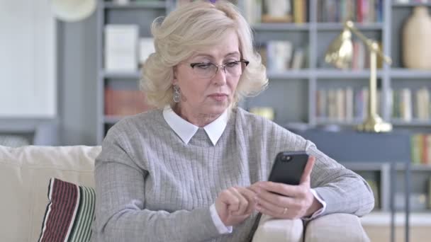 Traurige alte Frau vor dem Verlust ihres Smartphones — Stockvideo