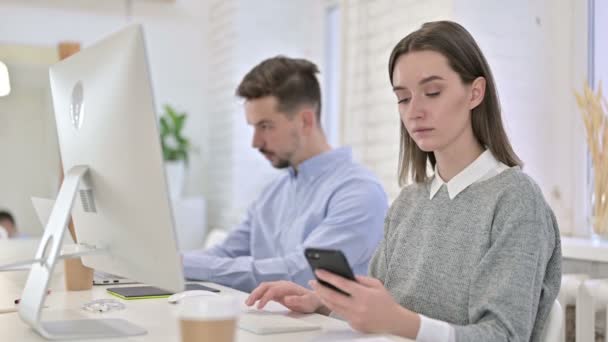 Atractiva mujer creativa usando Smartphone y trabajando en el escritorio — Vídeos de Stock