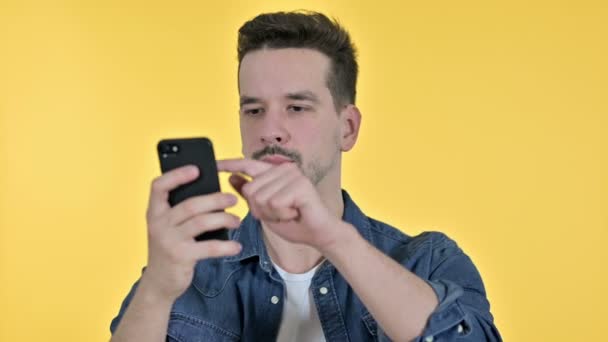 Портрет молодого человека, празднующего успех на смартфоне, желтый фон — стоковое видео