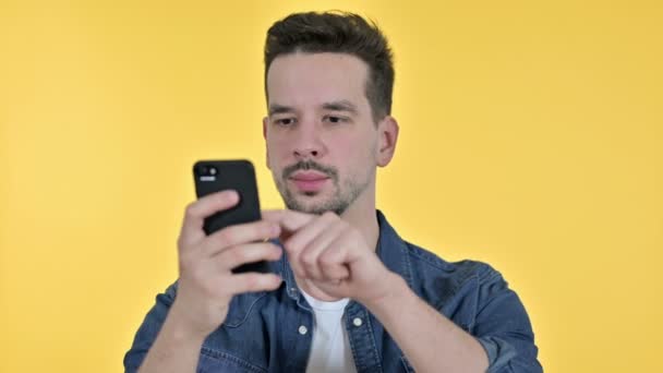 Портрет привлекательного молодого человека с помощью смартфона, желтого фона — стоковое видео