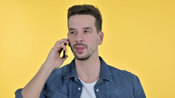 Портрет жизнерадостного молодого человека, говорящего на смартфоне, жёлтый фон — стоковое видео