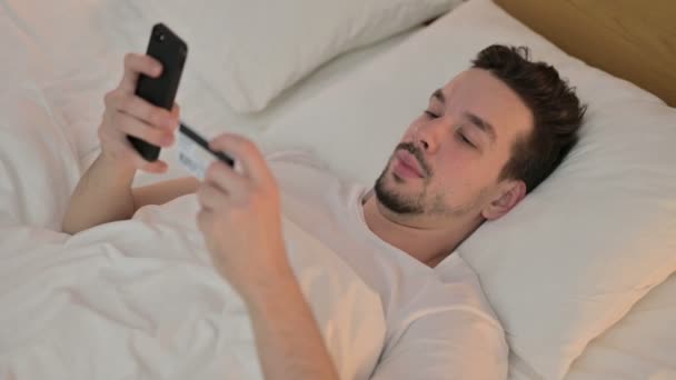Framgångsrik Online shopping av ung man på smartphone i sängen — Stockvideo
