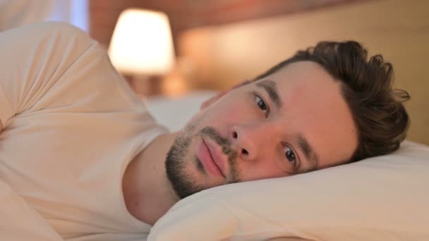 Портрет молодого человека, смотрящего на камеру в постели — стоковое видео