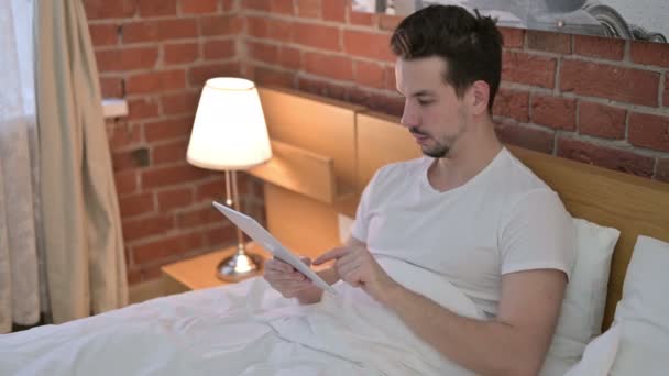 Амбициозный молодой человек использует планшет в постели — стоковое видео