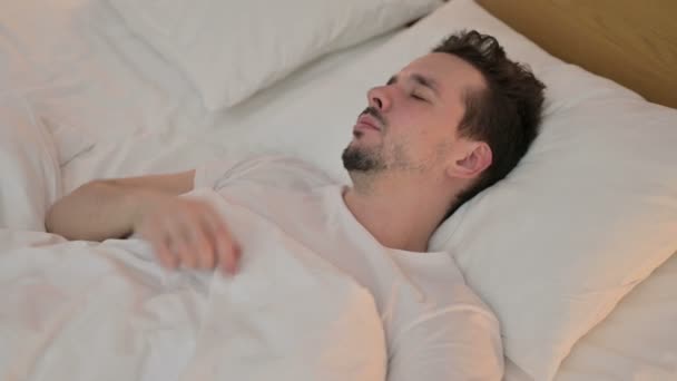 Уставший молодой человек пытается спать в постели — стоковое видео