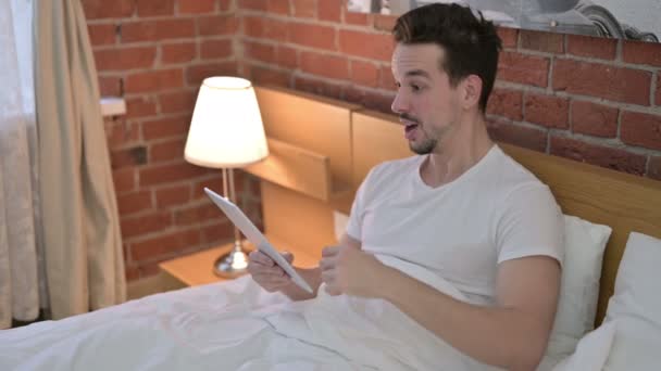 Jongeman viert succes op tablet in bed — Stockvideo