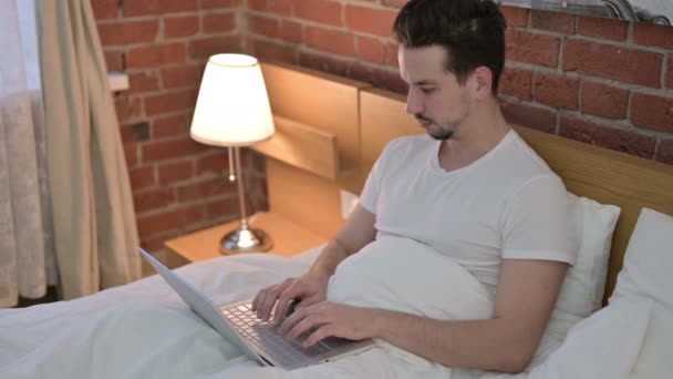 Joven ambicioso trabajando en el ordenador portátil en la cama — Vídeos de Stock