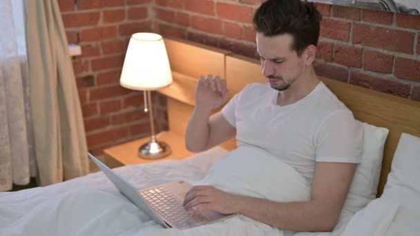 Ung man som har ont i nacken när du arbetar på laptop i sängen — Stockvideo