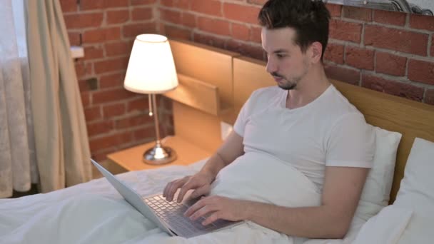 Mladý muž s bolestí hlavy při práci na notebooku v posteli — Stock video