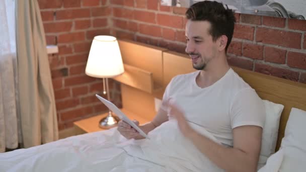 Jongeman doet videochat op tablet in bed — Stockvideo