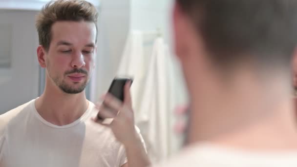 Jongeman aan het praten op smartphone in spiegel — Stockvideo