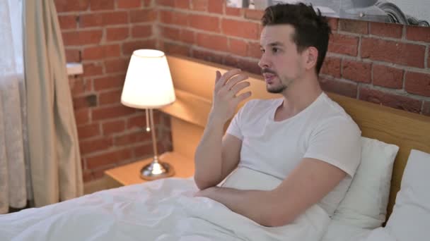 Rozrušený mladý muž sedí a stává se starosti v posteli — Stock video