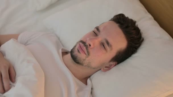 Portret van een jonge man met hoofdpijn in bed — Stockvideo