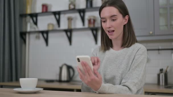自宅でスマートフォンで成功を祝う若い女性 — ストック動画