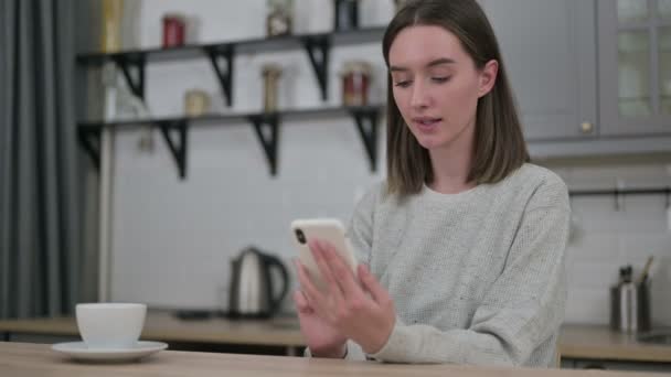 Jonge vrouw reageert op mislukking op smartphone in de woonkamer — Stockvideo