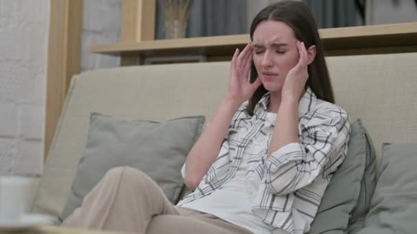 Vacker ung kvinna sitter på soffan och har huvudvärk — Stockvideo