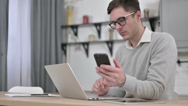 Mladý muž používající smartphone a notebook — Stock video
