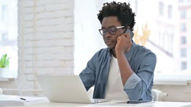 Ofiste akıllı telefondan konuşan genç Afrikalı adam.
