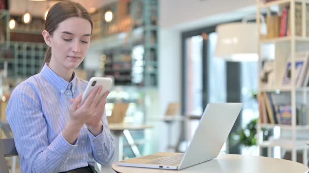 Smartphonegebruik door jonge zakenvrouw met laptop in Cafe — Stockvideo