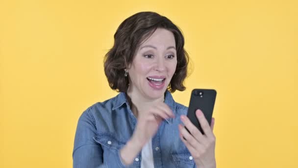 Mulher velha comemorando no Smartphone, fundo amarelo — Vídeo de Stock