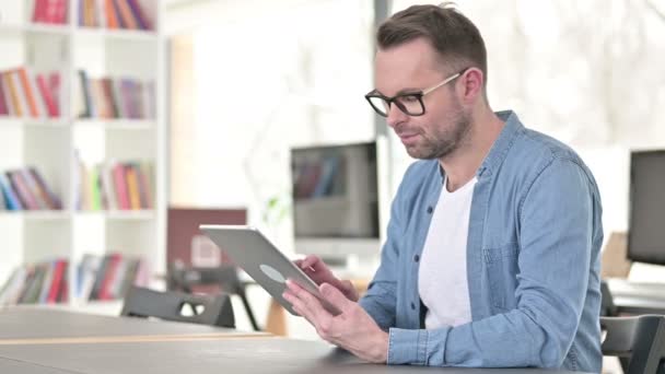 Молодой человек в очках с помощью планшета на работе — стоковое видео