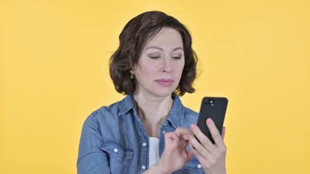 Old Woman with Loss on Smartphone, Yellow Background — Stock video