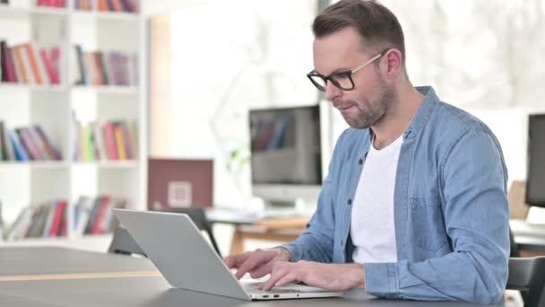 Homem jovem em óculos perturbado pela perda, usando laptop — Vídeo de Stock