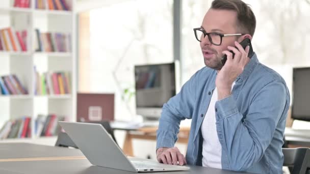 Junger Mann mit Brille spricht im Büro auf Smartphone — Stockvideo