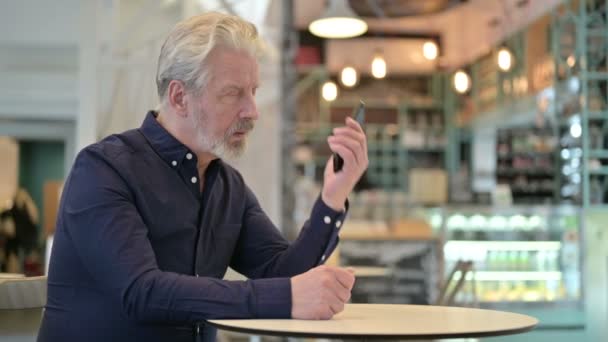 Старик разговаривает по смартфону в кафе — стоковое видео