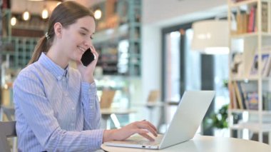 Genç İşkadını Kafe 'de dizüstü bilgisayarla telefonda konuşuyor.