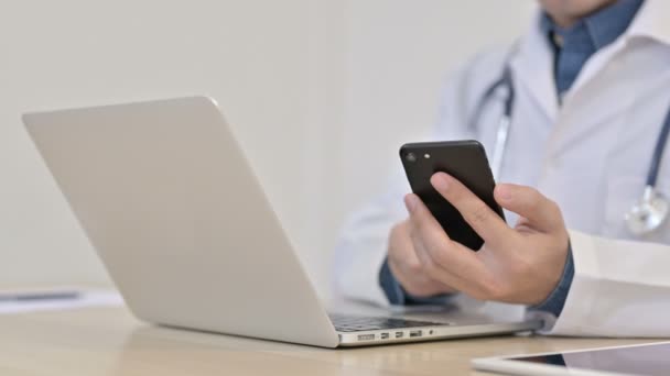 Manos del médico escribiendo en el teléfono inteligente con el ordenador portátil — Vídeo de stock
