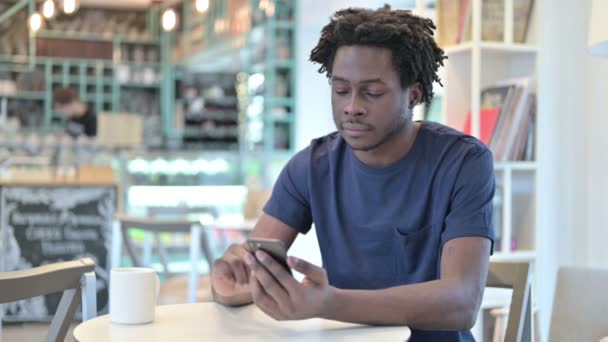 Hombre africano reaccionando a la pérdida en el teléfono inteligente en Café — Vídeos de Stock