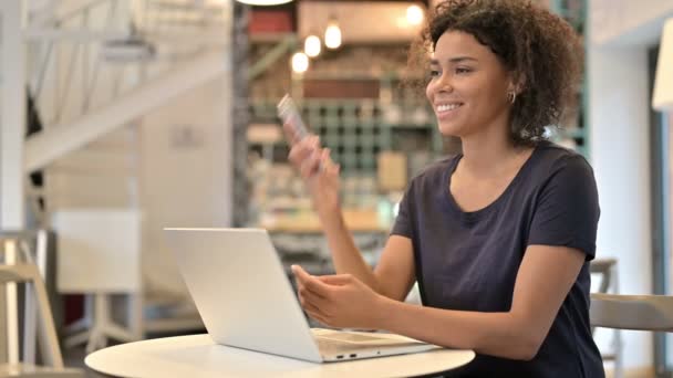 Молодая африканская женщина с ноутбуком разговаривает на смартфоне в кафе — стоковое видео