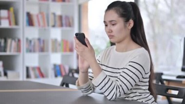 Kütüphanede Akıllı Telefon kullanan Ciddi Genç Asyalı Kadın 