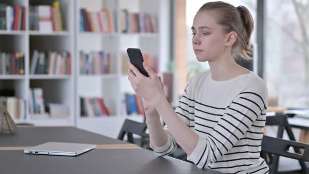 Smartphone-Nutzung durch junge Frau in Bibliothek — Stockvideo