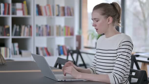 Giovane donna seria che utilizza il computer portatile, tosse in biblioteca — Video Stock