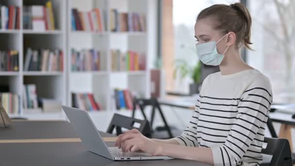 Jeune femme avec masque visage en utilisant un ordinateur portable dans la bibliothèque — Video