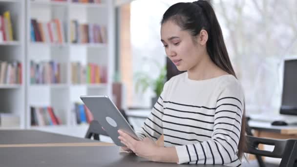 Mujer asiática joven celebrando el éxito en la tableta en la biblioteca — Vídeo de stock