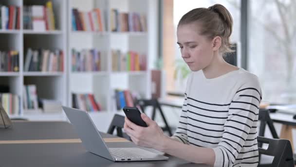 Uso smartphone da parte di Young Woman con computer portatile in biblioteca — Video Stock