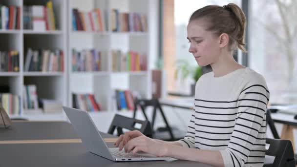 Laptopgebruik door jonge vrouw met hoofdpijn in bibliotheek — Stockvideo