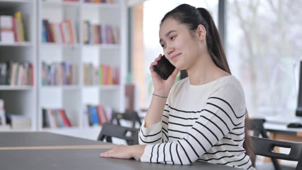 Schöne junge Asiatin spricht in Bibliothek über Smartphone — Stockvideo