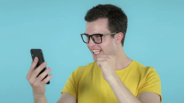 Uomo casual eccitato per il successo durante l'utilizzo di smartphone isolato su sfondo blu — Foto Stock