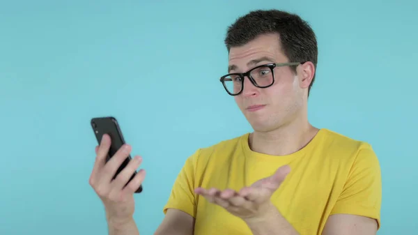 Hombre casual reaccionando a la pérdida y el uso de Smartphone aislado sobre fondo azul —  Fotos de Stock