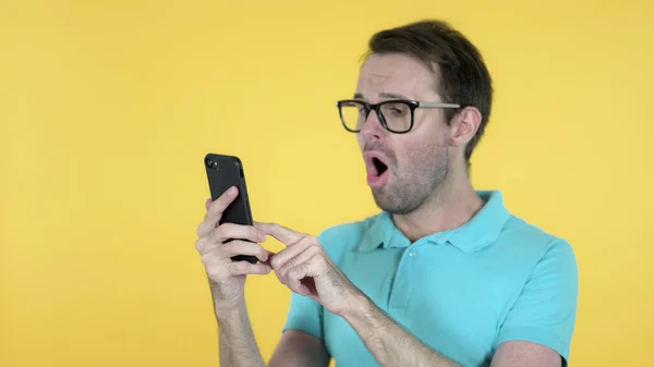 Hombre casual Emocionado por el éxito mientras se utiliza el teléfono inteligente aislado en el fondo amarillo —  Fotos de Stock