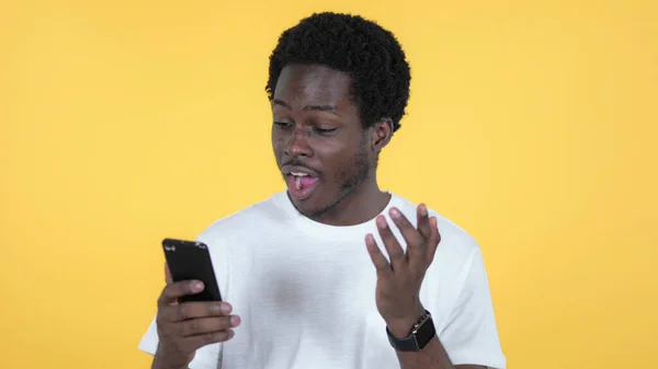 Šťastný příležitostný africký muž jásot překvapený úspěch na Smartphone izolované na žlutém pozadí — Stock fotografie