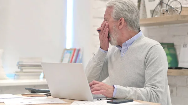 Vieil homme fatigué bâillant tout en utilisant un ordinateur portable — Photo