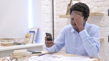 Stresli Afrikalı genç adam akıllı telefonunu kullanıyor.