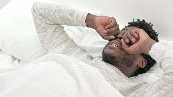 Молодой африканский человек просыпается в постели, потирая глаза — стоковое фото