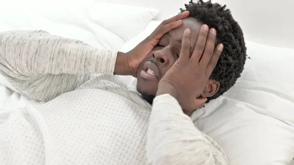 Mladý Afričan s bolestí hlavy v posteli — Stock fotografie